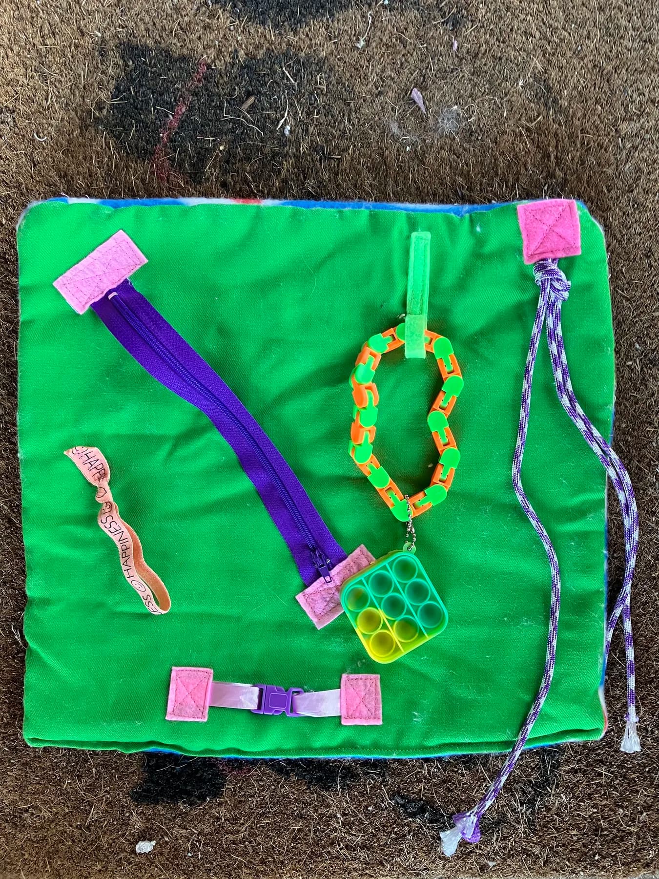Green activity blanket with tactile pieces, zippers, and textured details.